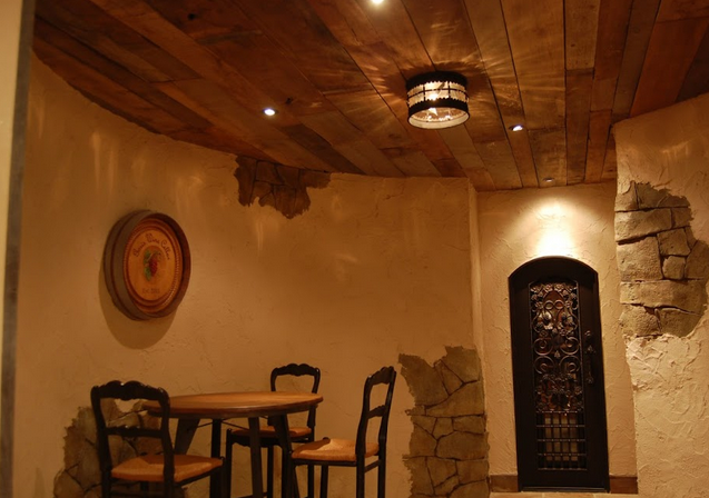 A wine tasting room with warm lighting, metal door, and wooden ceiling.