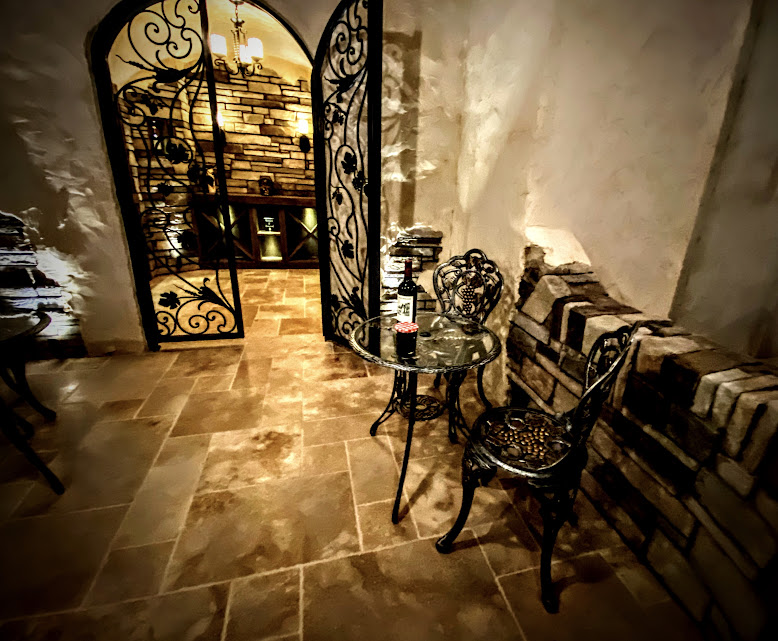 A rustic wine cellar hallway with wrought-iron doors, stone walls, and a small bistro table and chair