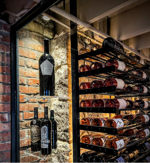 A stylish wine cellar display with neatly stacked bottles on metal racks beside a glass cabinet set against exposed brick walls